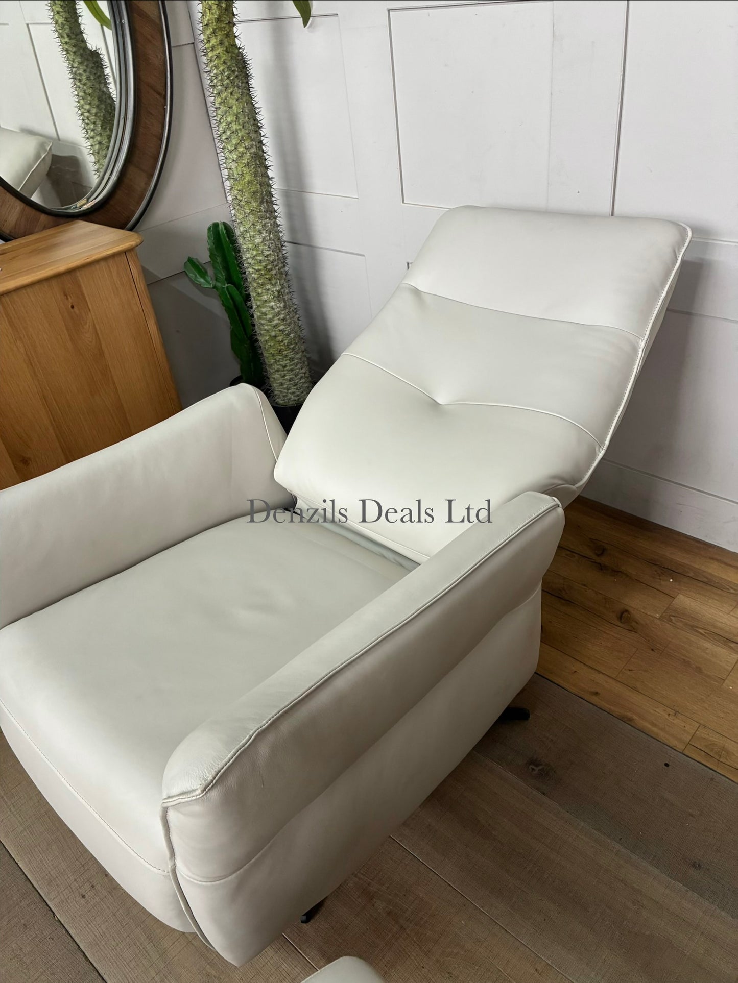 A contemporary living room reclining armchair paired with a matching rectangular footstool. Both pieces are covered in high-quality natural leather, showcasing unique organic textures, wrinkles, and characteristics. The set features a streamlined, padded frame resting on slim, minimalist black metal legs.