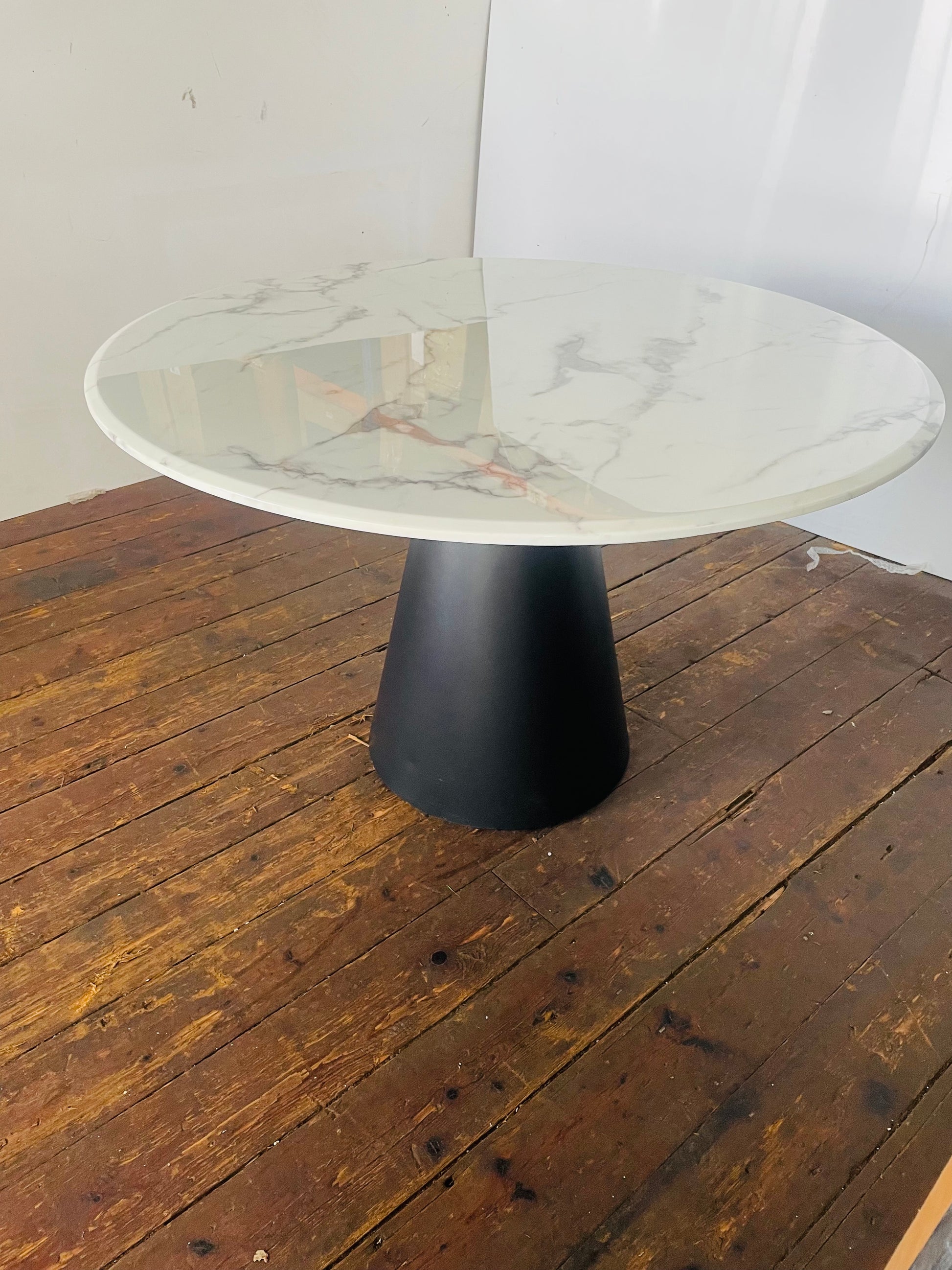 A 120cm round dining table by Richmond featuring a white faux-marble top and sleek black metal legs. 