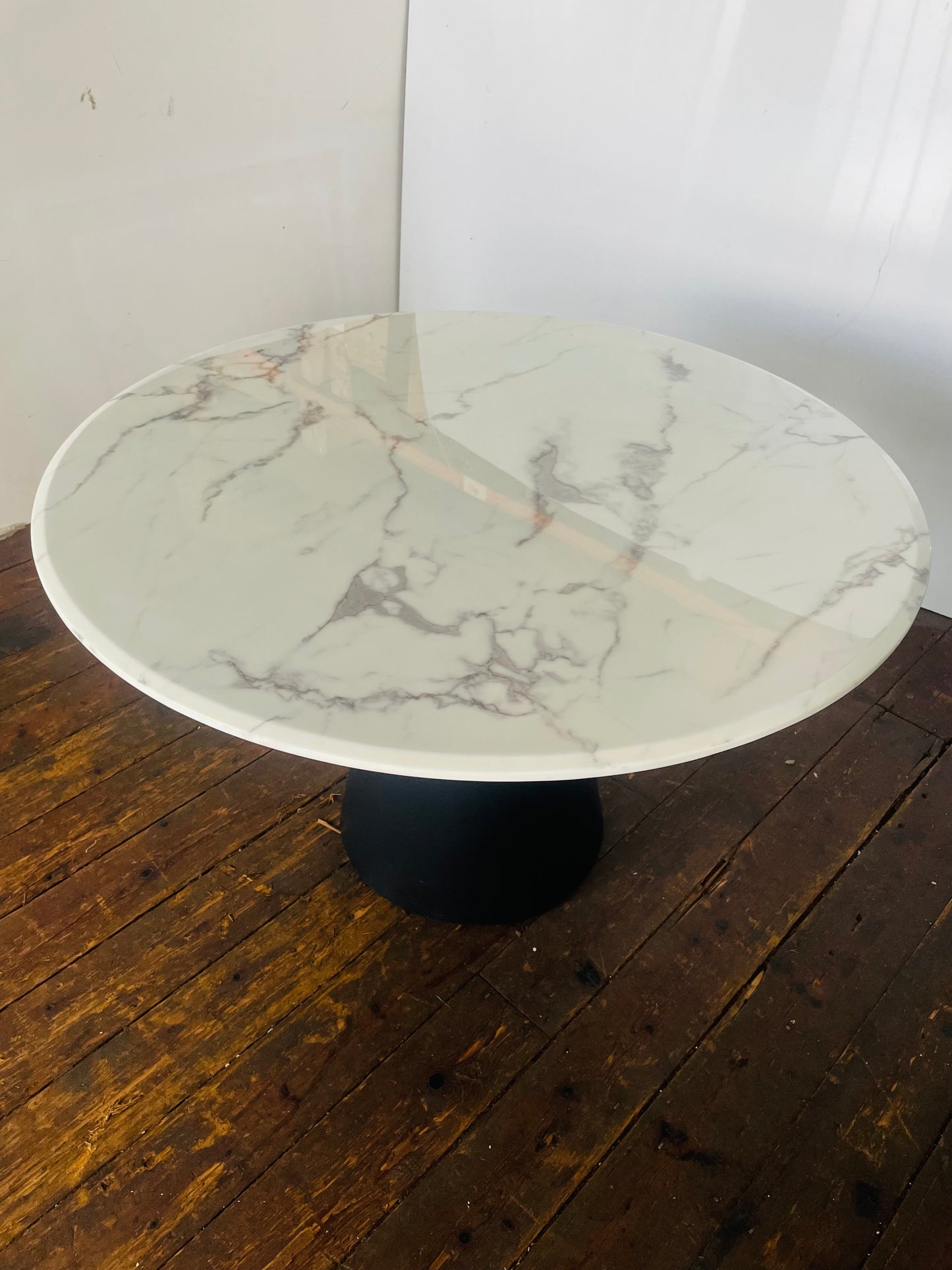 A 120cm round dining table featuring a white faux-marble top and sleek black metal legs. 