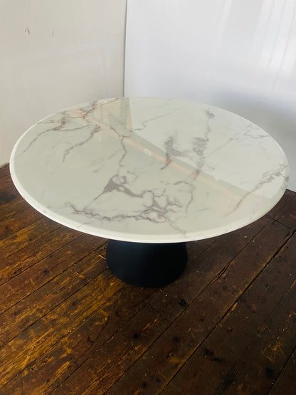 A 120cm round dining table featuring a white faux-marble top and sleek black metal legs. 