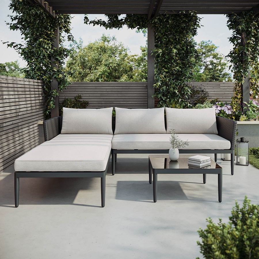A 4-seater black PE rattan outdoor corner sofa with an extended chaise section, light beige thick cushions, and a low square coffee table with a tempered glass top.