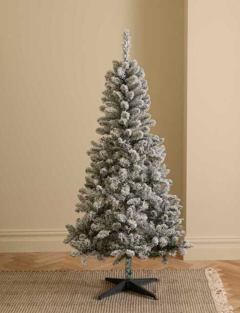 A 6-foot artificial M&S snowy spruce Christmas tree with a conical shape, dense green and white snow-dusted branches, and a quick-fit plastic stand