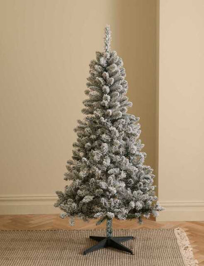 A 6-foot artificial M&S snowy spruce Christmas tree with a conical shape, dense green and white snow-dusted branches, and a quick-fit plastic stand