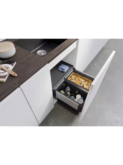 A BLANCO Select under-counter pull-out kitchen bin with two grey compartments, shown partially extended from a minimalist dark cabinet to reveal its 38-litre waste separation system. 