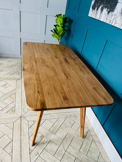 A Scandi-inspired minimalist 4-seater dining table by John Lewis, crafted from American oak wood with a visible natural grain, an oiled finish, and tapered legs.