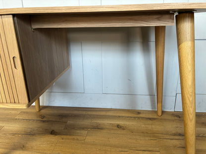 A compact John Lewis Grayson writing desk made of light oak, featuring spindle-shaped tapered legs, a smooth rectangular work surface, and a built-in storage cabinet on the right with a distinctive Scandinavian-style slatted sliding door.