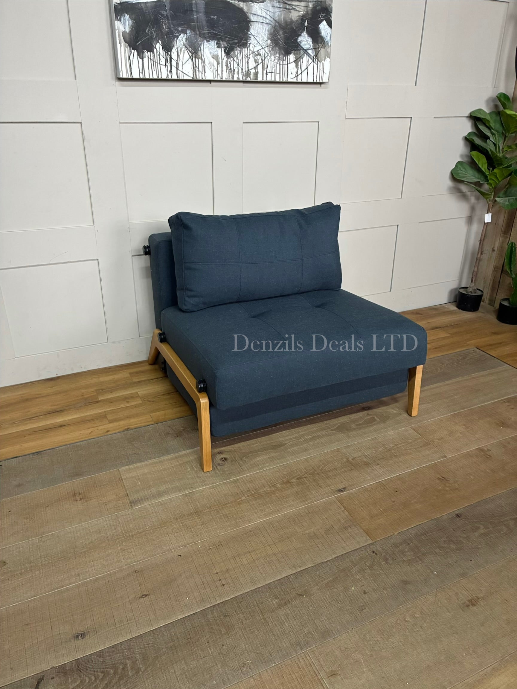 A compact, modern armchair bed by Innovation Living upholstered in dark Nist Blue fabric, featuring a tufted back cushion and sleek metal legs.