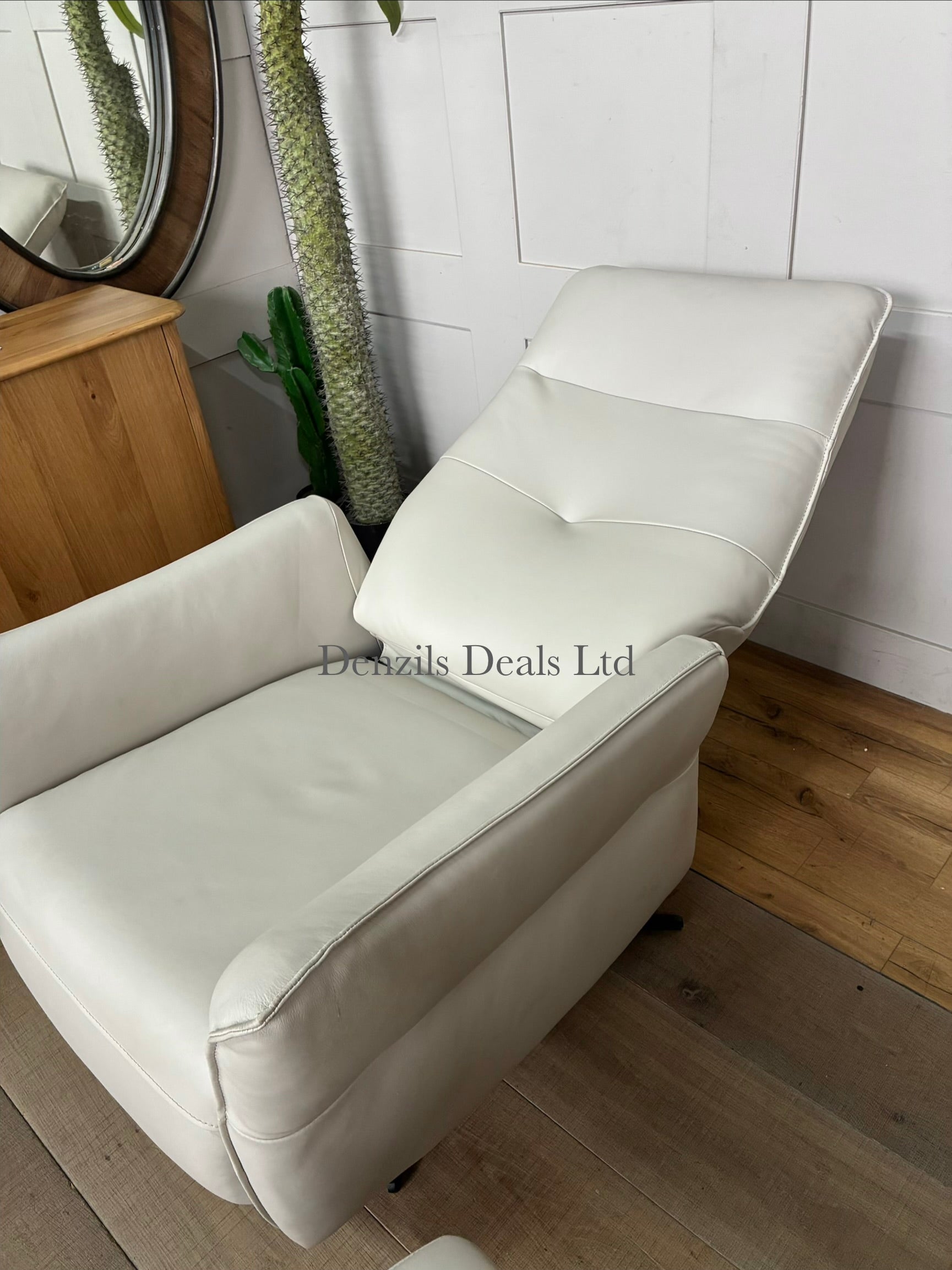 A contemporary living room reclining armchair paired with a matching rectangular footstool. Both pieces are covered in high-quality natural leather, showcasing unique organic textures, wrinkles, and characteristics. The set features a streamlined, padded frame resting on slim, minimalist black metal legs.