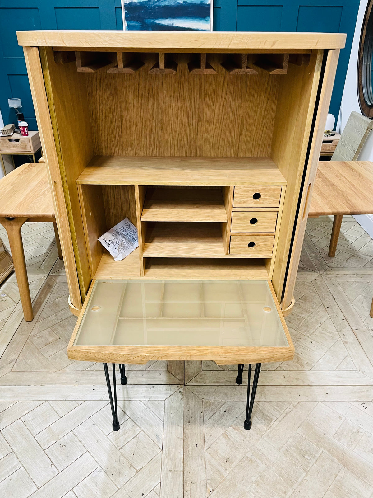 A contemporary Tambour collection hideaway desk top unit in a grey waxed wood finish, featuring flexible slatted sliding doors pulled back to show internal storage space, shown with removable legs