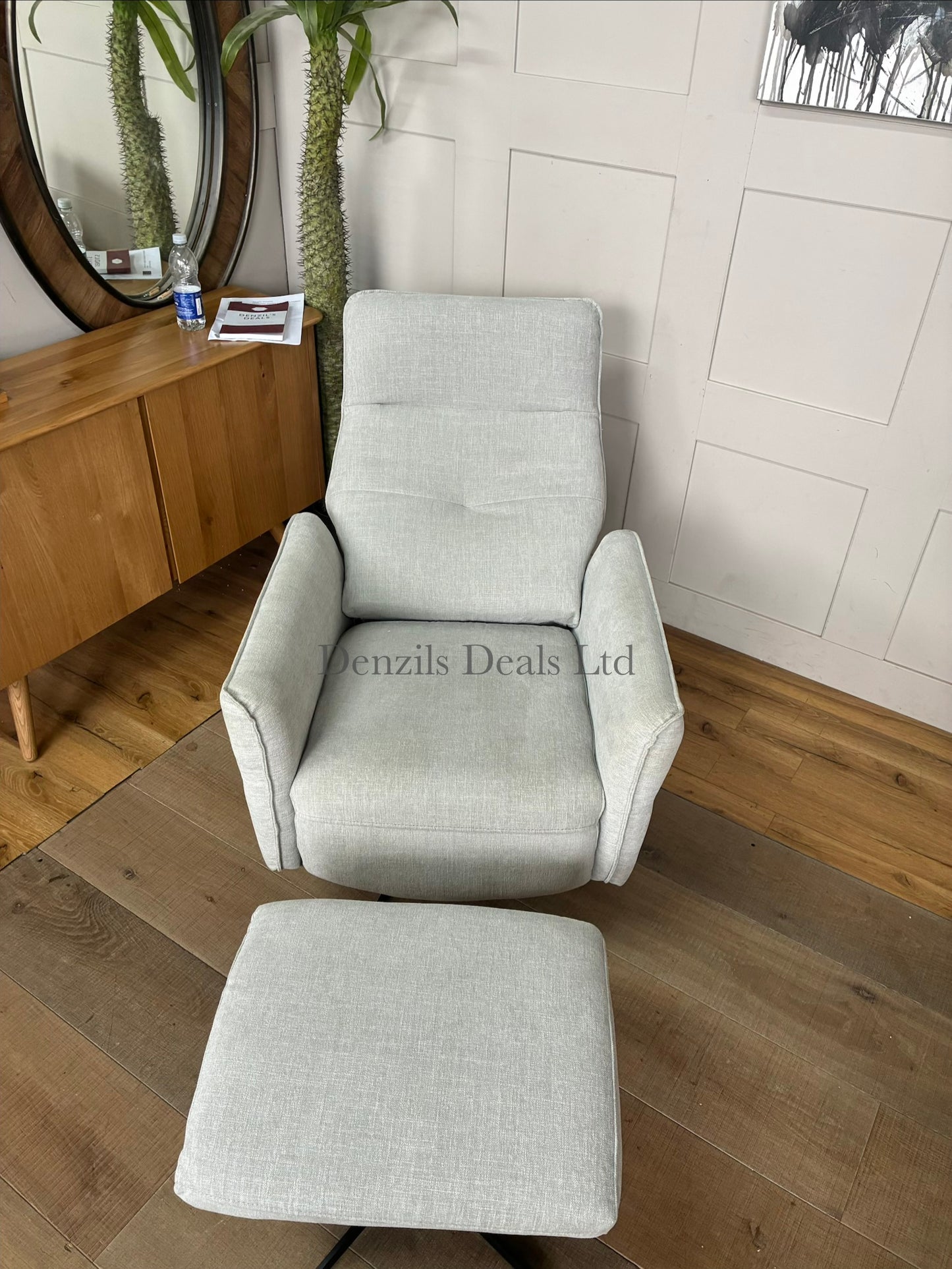 A contemporary ergonomic armchair and footstool set featuring a plush, high-back silhouette covered in textured light grey chenille upholstery. The set is elevated on sleek, angular black metal legs, showcasing a comfortable, modern look for a living room or study.