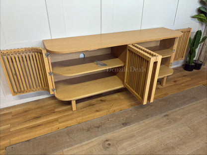 A contemporary light oak wood TV stand sideboard with a curved, capsule-shaped frame. The unit features four cupboard doors with a textured vertical slatted design and seamless, minimalist wooden handles. It sits slightly raised off the floor on a solid base.