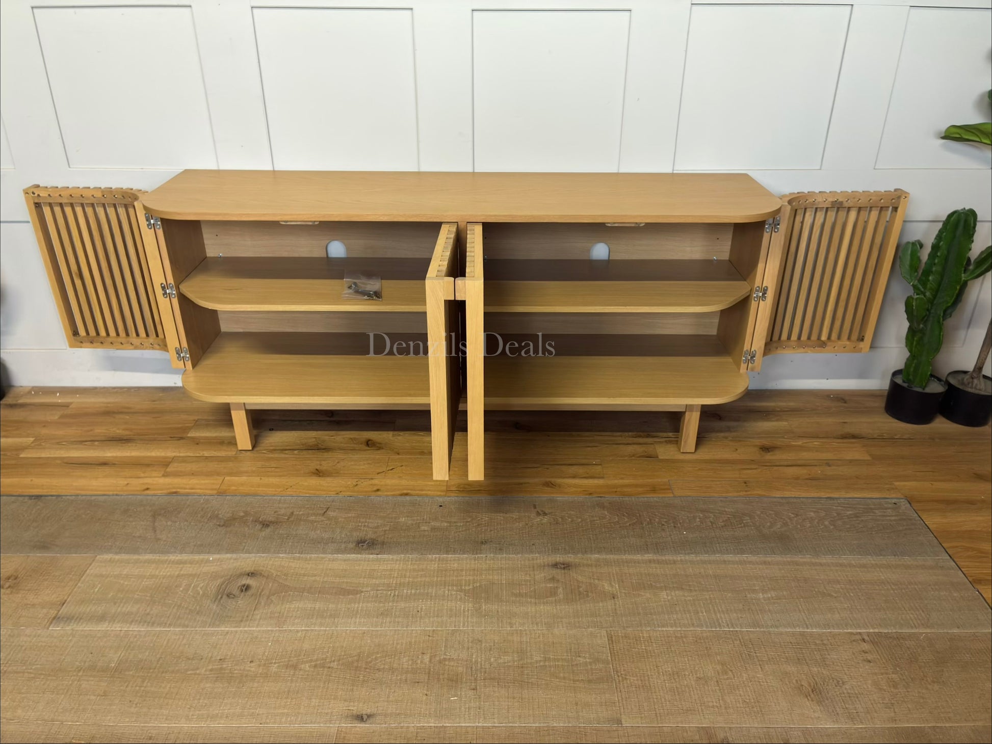 A contemporary light oak wood TV stand sideboard with a curved, capsule-shaped frame. The unit features four cupboard doors with a textured vertical slatted design and seamless, minimalist wooden handles. It sits slightly raised off the floor on a solid base.