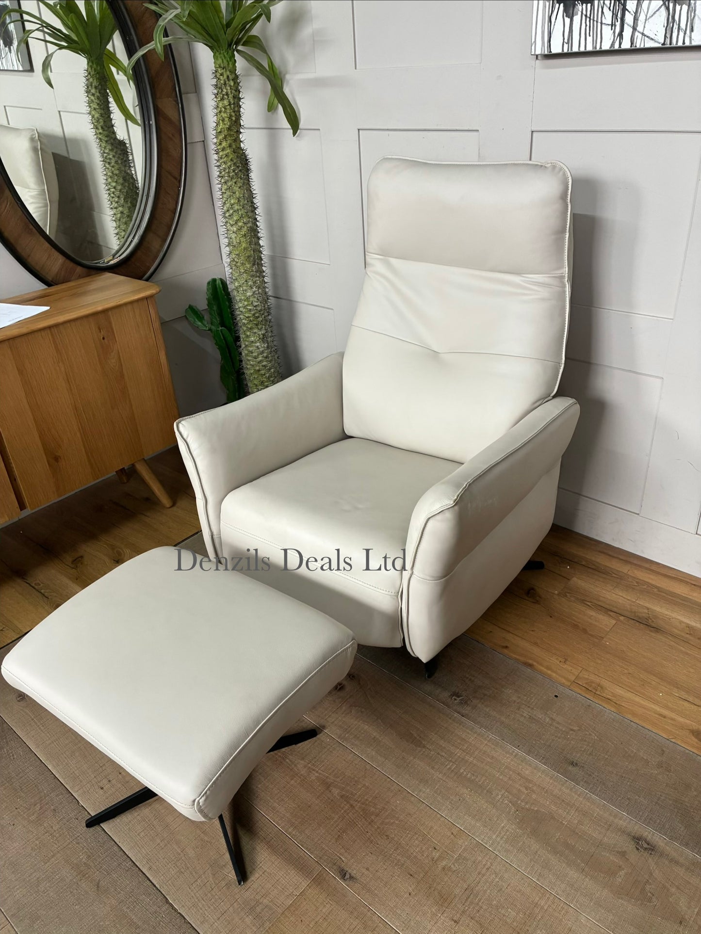 A contemporary living room reclining armchair paired with a matching rectangular footstool. Both pieces are covered in high-quality natural leather, showcasing unique organic textures, wrinkles, and characteristics. The set features a streamlined, padded frame resting on slim, minimalist black metal legs.