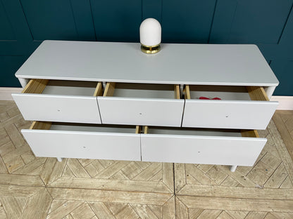 A contemporary, soft-profile John Lewis Spindle 7 Drawer Chest in a smooth grey lacquered finish. The spacious wooden chest features a combination of deep and shallow drawers arranged vertically, built with sturdy pine and MDF. It is designed with clean lines and distinctly rounded edges that soften its overall profile, offering a modern and minimalist look for a bedroom.
