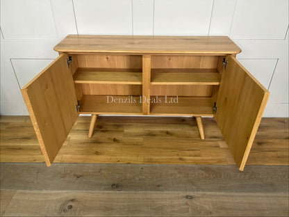 A contemporary two-door wooden sideboard from the John Lewis Greenwood range. The cabinet is crafted from light-toned solid oak and oak veneers, featuring a pale Bianco oiled finish that highlights the natural, linear wood grain. It has a clean, minimalist rectangular shape, flat-fronted double doors with subtle integrated handles, and sits flat against the floor.
