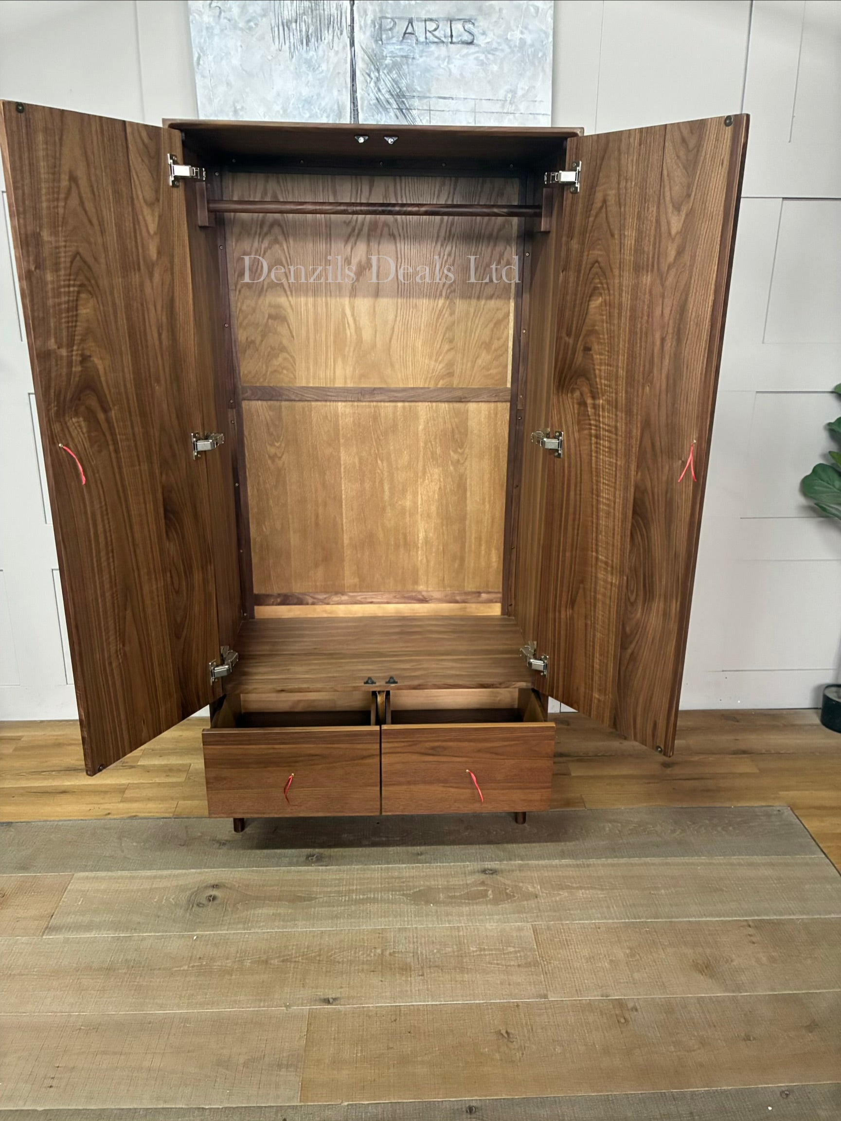 A freestanding mid-century modern style wardrobe crafted from dark walnut wood. It features two large cabinet doors with integrated vertical wooden handles, a single full-width storage drawer at the base, and short tapered legs providing under-cabinet clearance.
