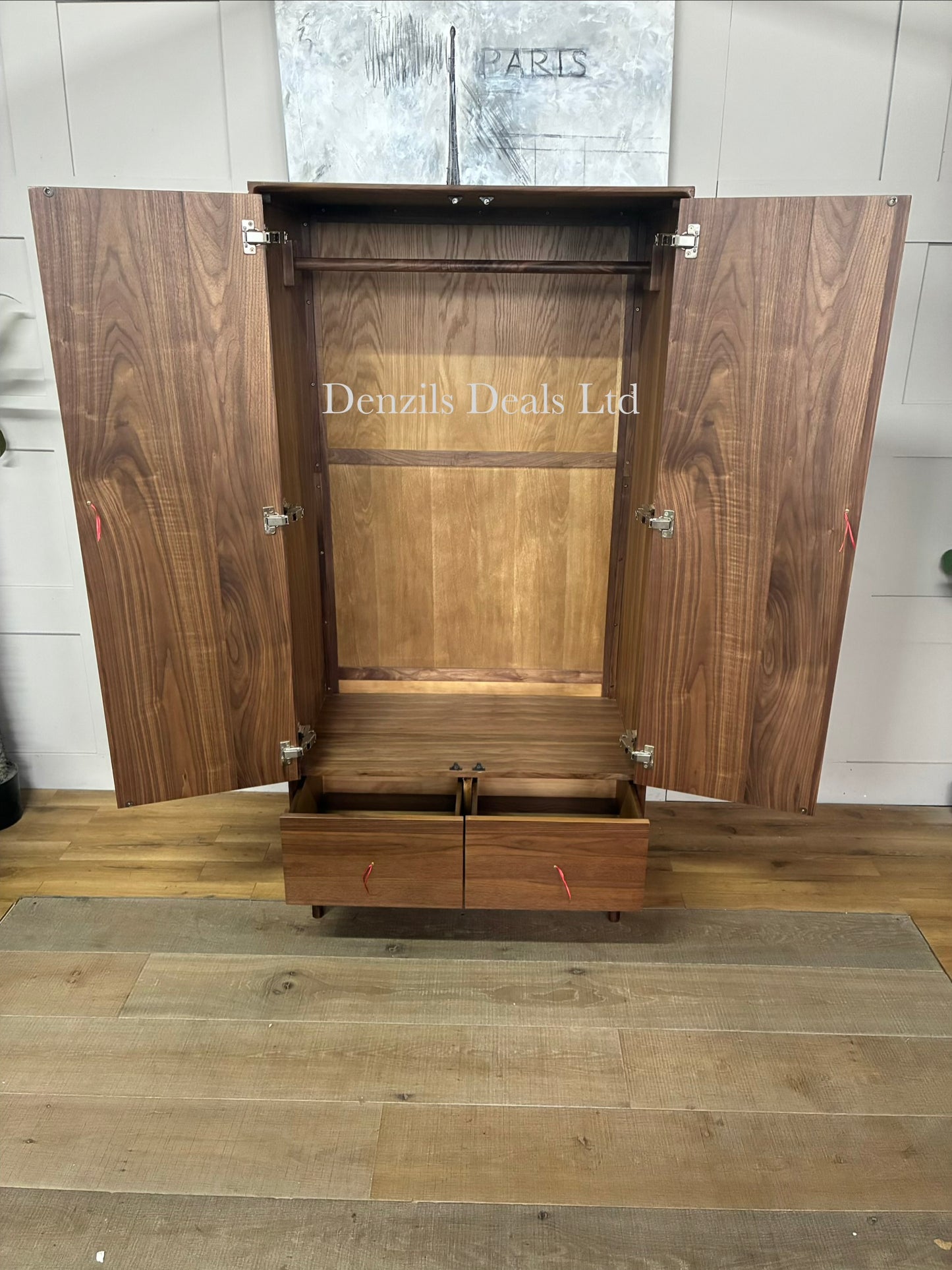 A freestanding mid-century modern style wardrobe crafted from dark walnut wood. It features two large cabinet doors with integrated vertical wooden handles, a single full-width storage drawer at the base, and short tapered legs providing under-cabinet clearance.