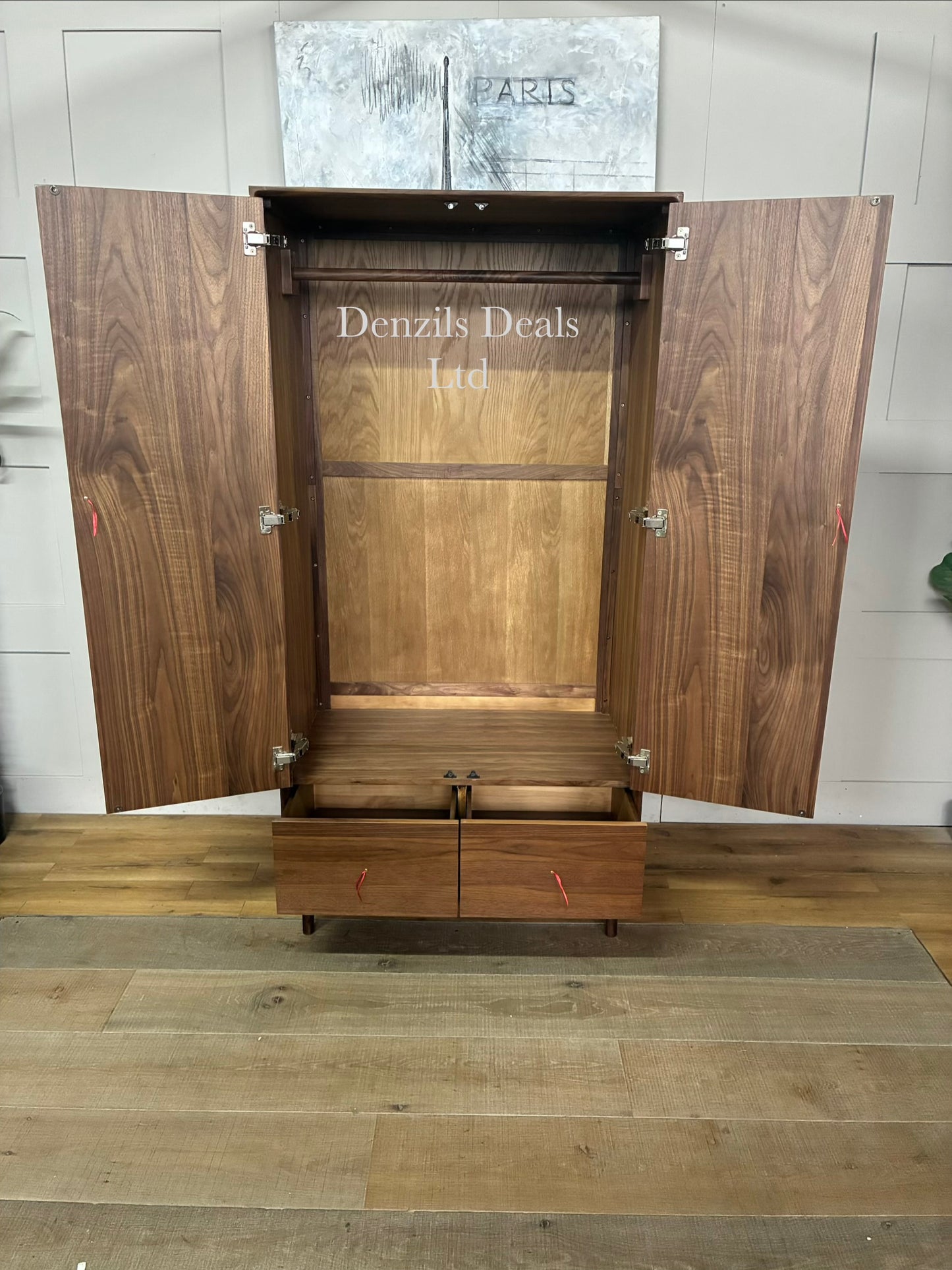 A freestanding mid-century modern style wardrobe crafted from dark walnut wood. It features two large cabinet doors with integrated vertical wooden handles, a single full-width storage drawer at the base, and short tapered legs providing under-cabinet clearance.