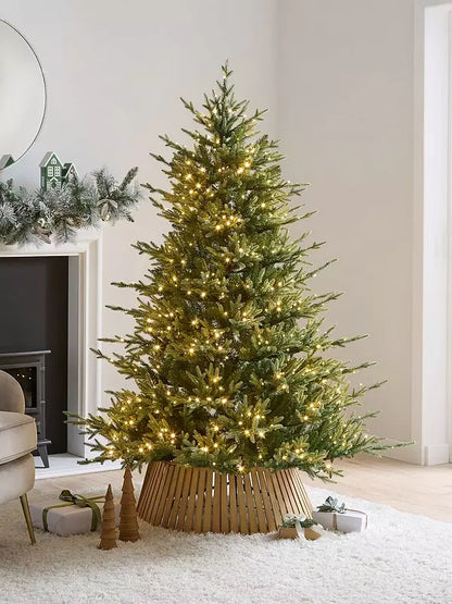 A full and dense 6ft artificial Grand Nottingham Fir Christmas tree styled in a cozy living room. The tree features highly realistic green foliage with 3,742 branch tips, warmly illuminated by 600 built-in warm white LED lights that cast a soft, festive glow