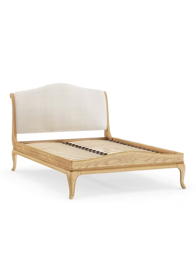 A grand, super king-size wooden sleigh bed frame crafted from solid oak with a warm, natural lacquered grain. The bed features a tall, gently scrolled headboard with traditional French-style carvings and a matching low-end footboard that curves subtly outward