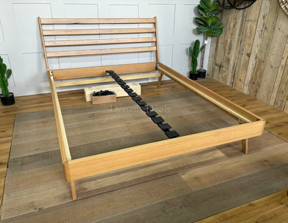 A king-size minimalist platform bed frame made of light natural oak wood. It features a high, slatted headboard with clean horizontal lines, tapered angled legs, and a sturdy sprung-slat base.