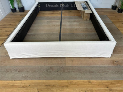 A king-size modern bedroom setup featuring the John Lewis Relax Rustic Upholstered Bed Frame. The bed has a tall, well-padded rectangular headboard covered in loose, casual-fitting natural beige fabric. The frame is built from visible timber feet at the base, supporting a low-profile matching upholstered surround