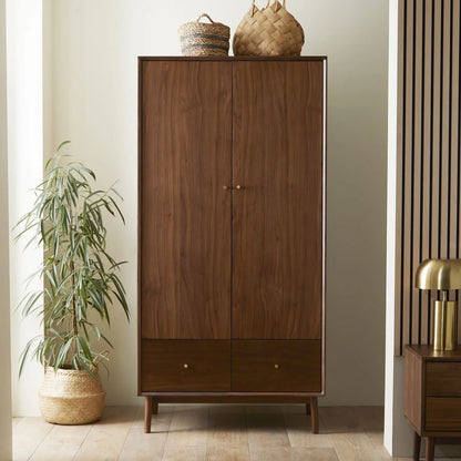 A mid-century modern two-door wooden wardrobe in a rich American walnut finish, featuring streamlined cabinet doors, polished brass knobs, and integrated base drawers