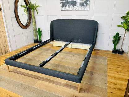 A modern John Lewis Show-Wood King Size Bed Frame covered in a cozy, textured brushed tweed charcoal fabric with a soft herringbone pattern. The bed features a gently curved, padded headboard and a sleek, exposed light wood frame running along the bottom and legs
