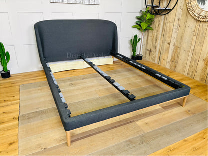 A modern John Lewis Show-Wood King Size Bed Frame covered in a cozy, textured brushed tweed charcoal fabric with a soft herringbone pattern. The bed features a gently curved, padded headboard and a sleek, exposed light wood frame running along the bottom and legs