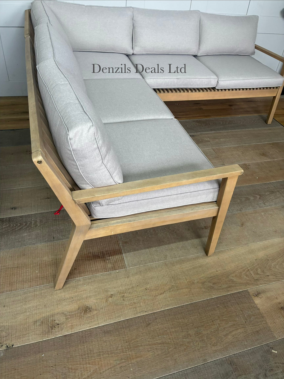 A modern L-shaped outdoor corner sofa from the John Lewis Mona range. The frame is crafted from light-toned natural acacia wood featuring a slatted design with angled legs and rounded corners. It is topped with thick, woven, shower-resistant seat and backrest cushions with clean piped edges
