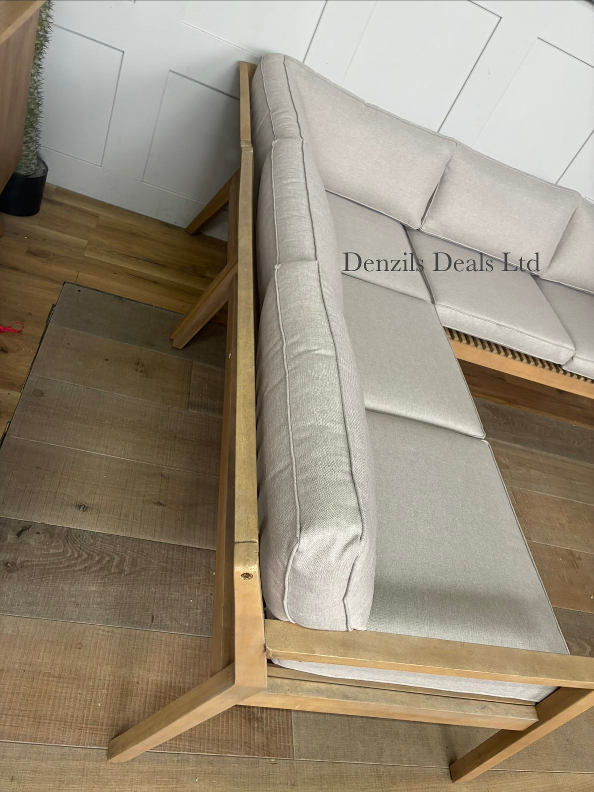 A modern L-shaped outdoor corner sofa from the John Lewis Mona range. The frame is crafted from light-toned natural acacia wood featuring a slatted design with angled legs and rounded corners. It is topped with thick, woven, shower-resistant seat and backrest cushions with clean piped edges