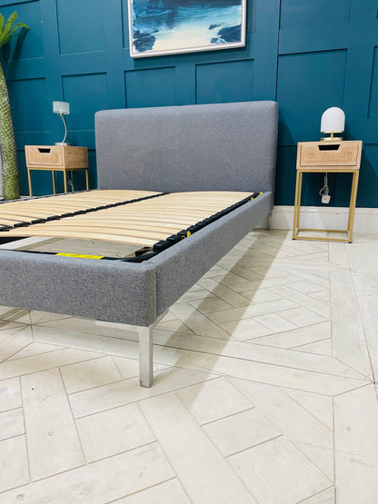 A modern Loaf double bed upholstered in a soft grey fabric with a lined, padded headboard and matching low footboard, set within a bright chrome metal frame.