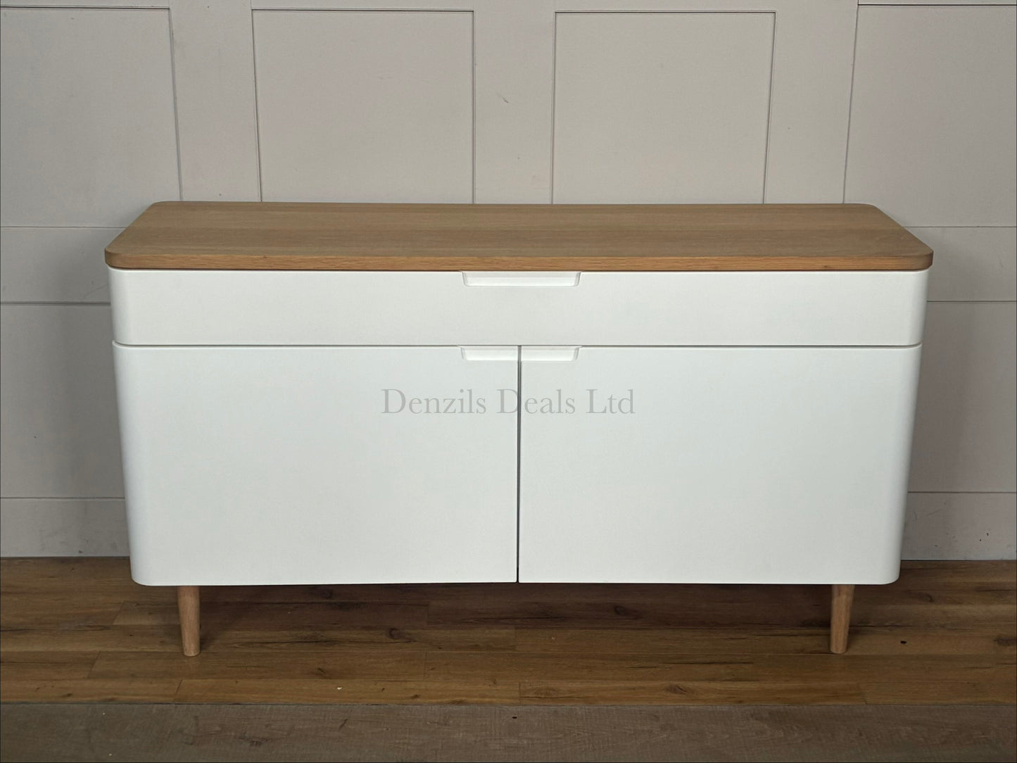 A modern Scandinavian-style wide sideboard featuring a matte white cabinet body, two doors, and a natural solid oak top surface with matching tapered wooden legs.