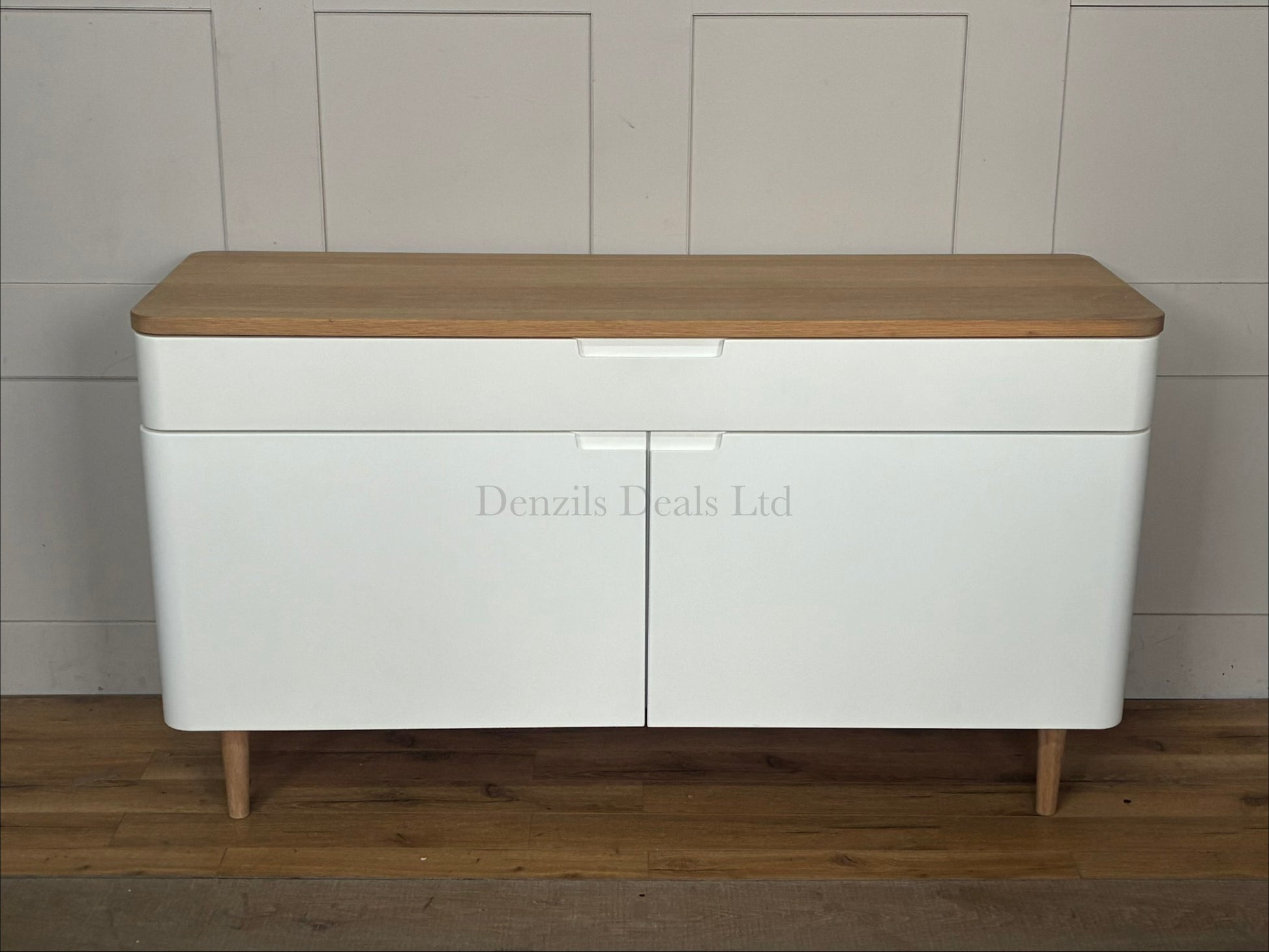 A modern Scandinavian-style wide sideboard featuring a matte white cabinet body, two doors, and a natural solid oak top surface with matching tapered wooden legs.