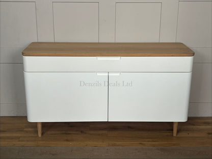 A modern Scandinavian-style wide sideboard featuring a matte white cabinet body, two doors, and a natural solid oak top surface with matching tapered wooden legs.
