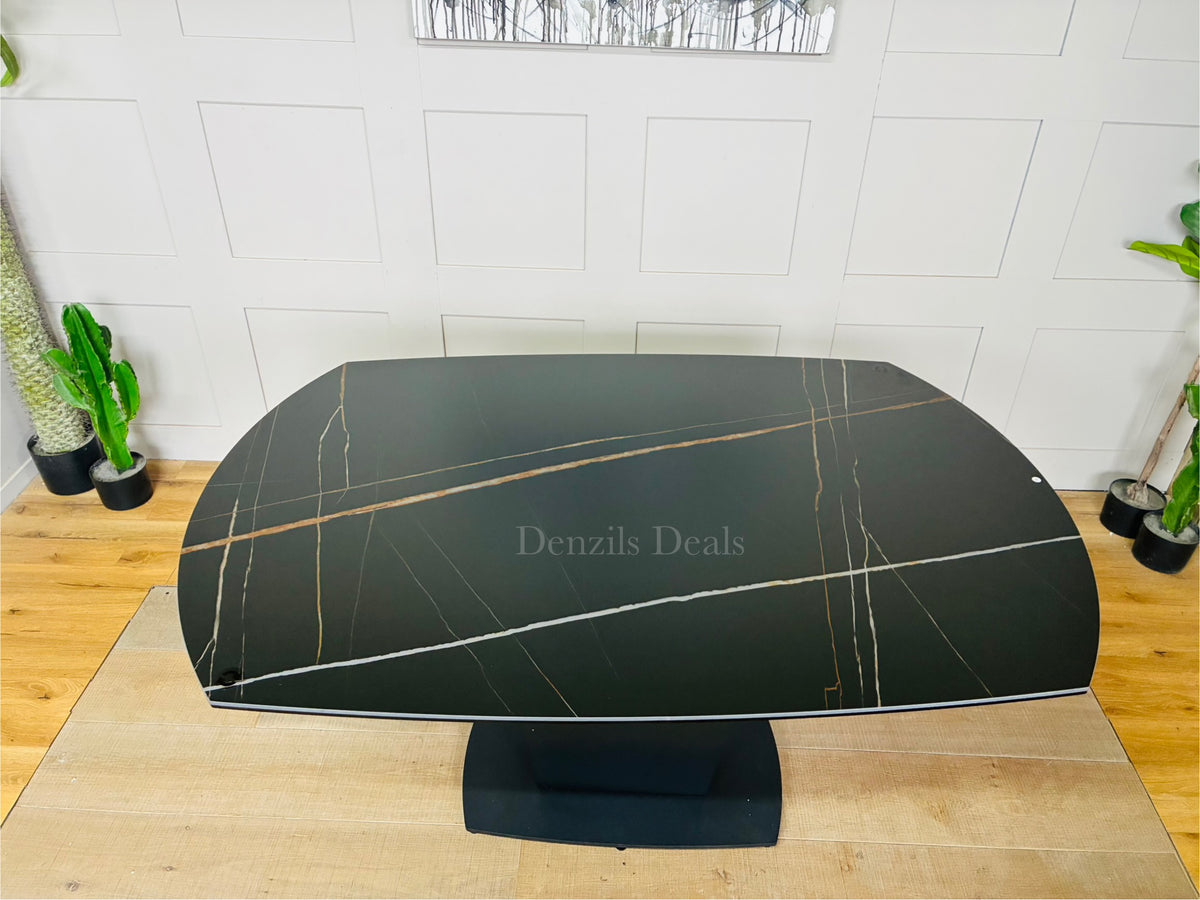 A modern black ceramic dining table with a distinctive white-veined marble effect. The table features an extendable top and a sleek, curved fiberglass tulip-style pedestal base. 