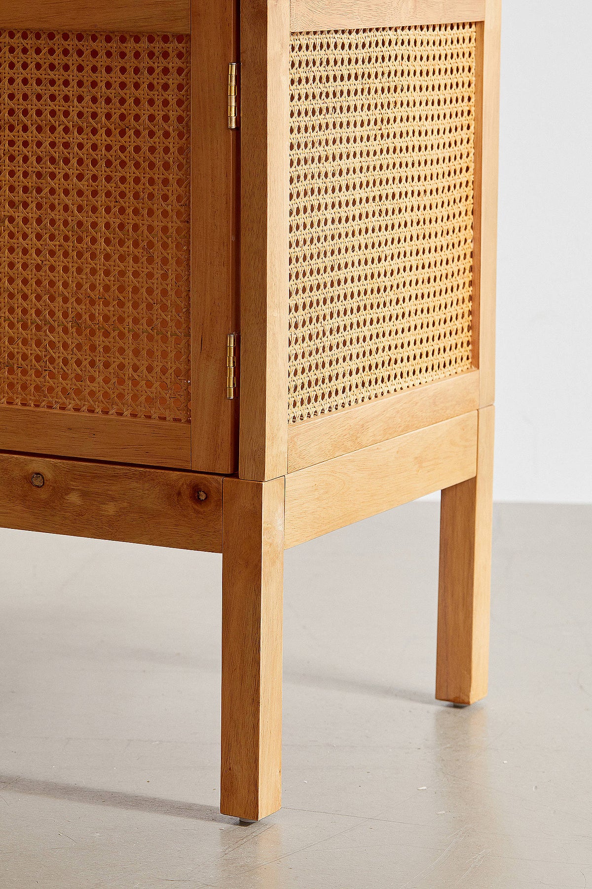 A modern bohemian TV stand made of light wood veneer and cane rattan panels. It features two cabinet doors with woven rattan fronts, small block handles, and tall, slim tapered legs