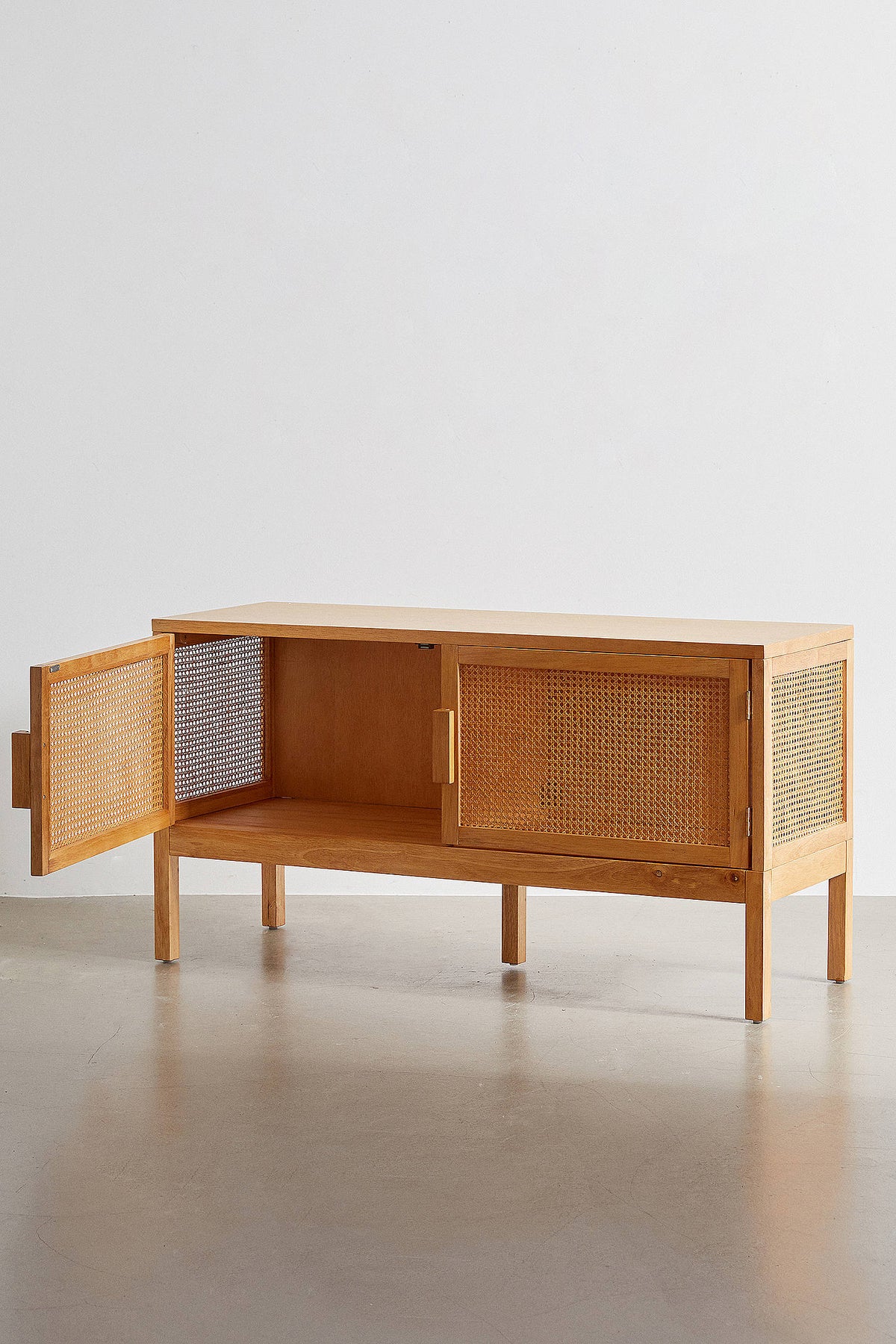 A modern bohemian TV stand made of light wood veneer and cane rattan panels. It features two cabinet doors with woven rattan fronts, small block handles, and tall, slim tapered legs