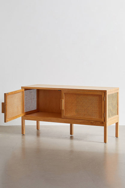 A modern bohemian TV stand made of light wood veneer and cane rattan panels. It features two cabinet doors with woven rattan fronts, small block handles, and tall, slim tapered legs