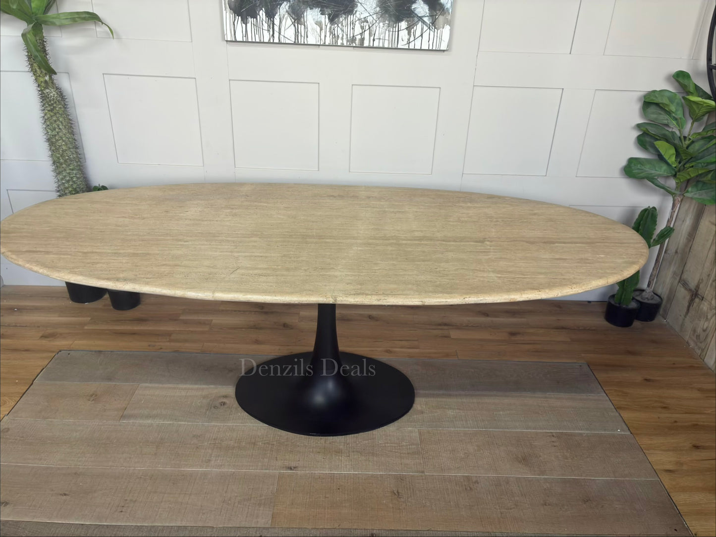 A modern dining room table by Richmond Interiors from the Hampton collection, featuring a large oval beige travertine tabletop with unique natural veining, supported by a sleek, black powder-coated iron base