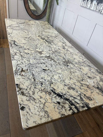 A rectangular Anthropologie Renata dining table with a thick, polished white marble top. The table is supported by thick, cylindrical wooden legs featuring a vertical fluted texture and a warm oak finish.