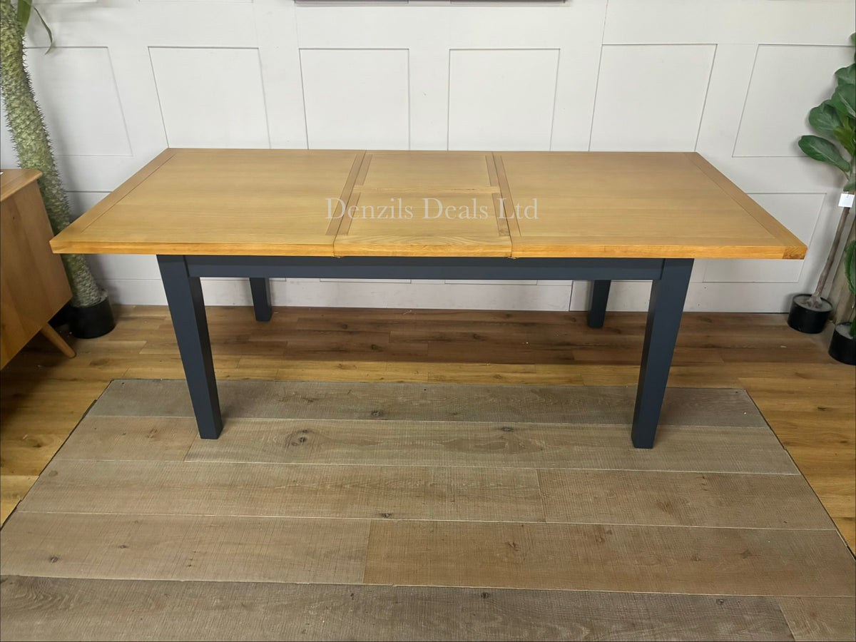 A rectangular wooden extending dining table from the DFS Country Living Maud range. The table features a premium navy blue painted finish on its sturdy legs and frame, contrasted by a smooth, natural oak wood grain tabletop with subtly rounded corners