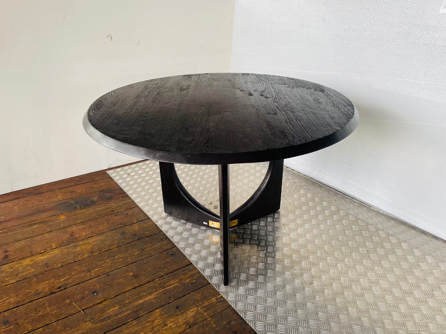 A round Anthropologie Iris dining table in a matte black oak finish, featuring a sculptural, curved pedestal base accented with gold-toned brass hardware