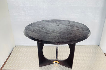 A round, black oak wood Anthropologie Iris dining table featuring a modern, sculptural silhouette with curved lines