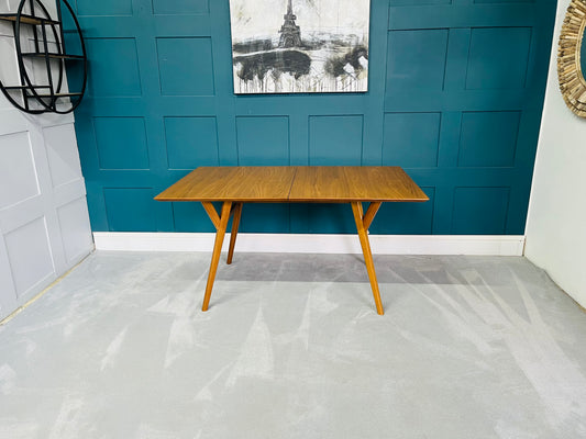A round, mid-century modern wooden dining table in an acorn finish featuring slender, tapered A-frame legs and a smooth veneer top."