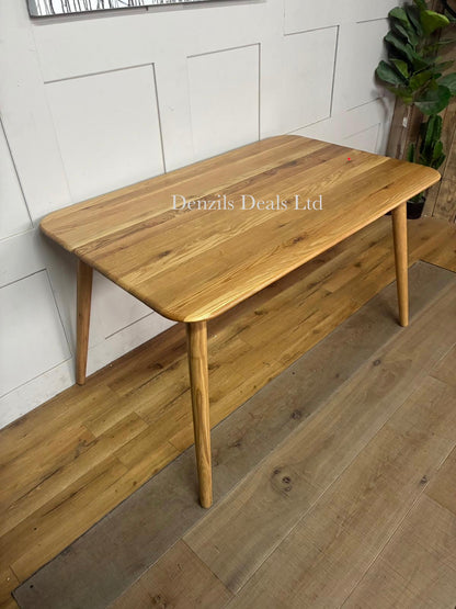A round wooden dining table with a smooth solid oak top finished in a light bianco oil, supported by simple wooden legs