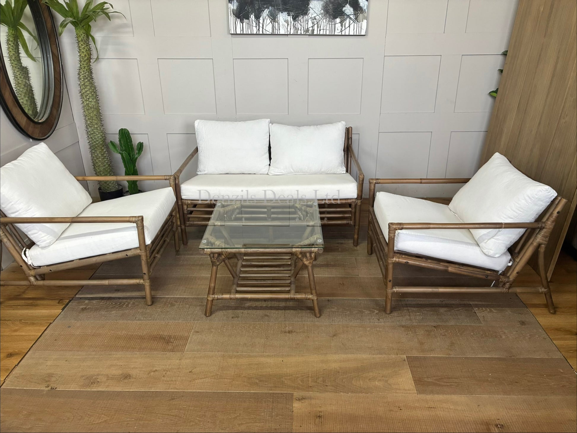 A soil-brown bamboo conservatory lounge set including a two-seater sofa, two matching armchairs, and a square glass-topped coffee table. The open-frame bamboo features plush, off-white canvas cushions.