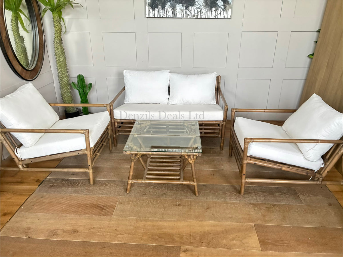 A soil-brown bamboo conservatory lounge set including a two-seater sofa, two matching armchairs, and a square glass-topped coffee table. The open-frame bamboo features plush, off-white canvas cushions.