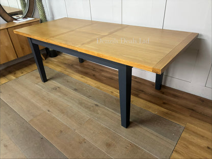 A traditional dining room featuring the DFS Country Living Maud navy extending dining table, showcasing its rustic dark blue frame and natural wood tabletop,