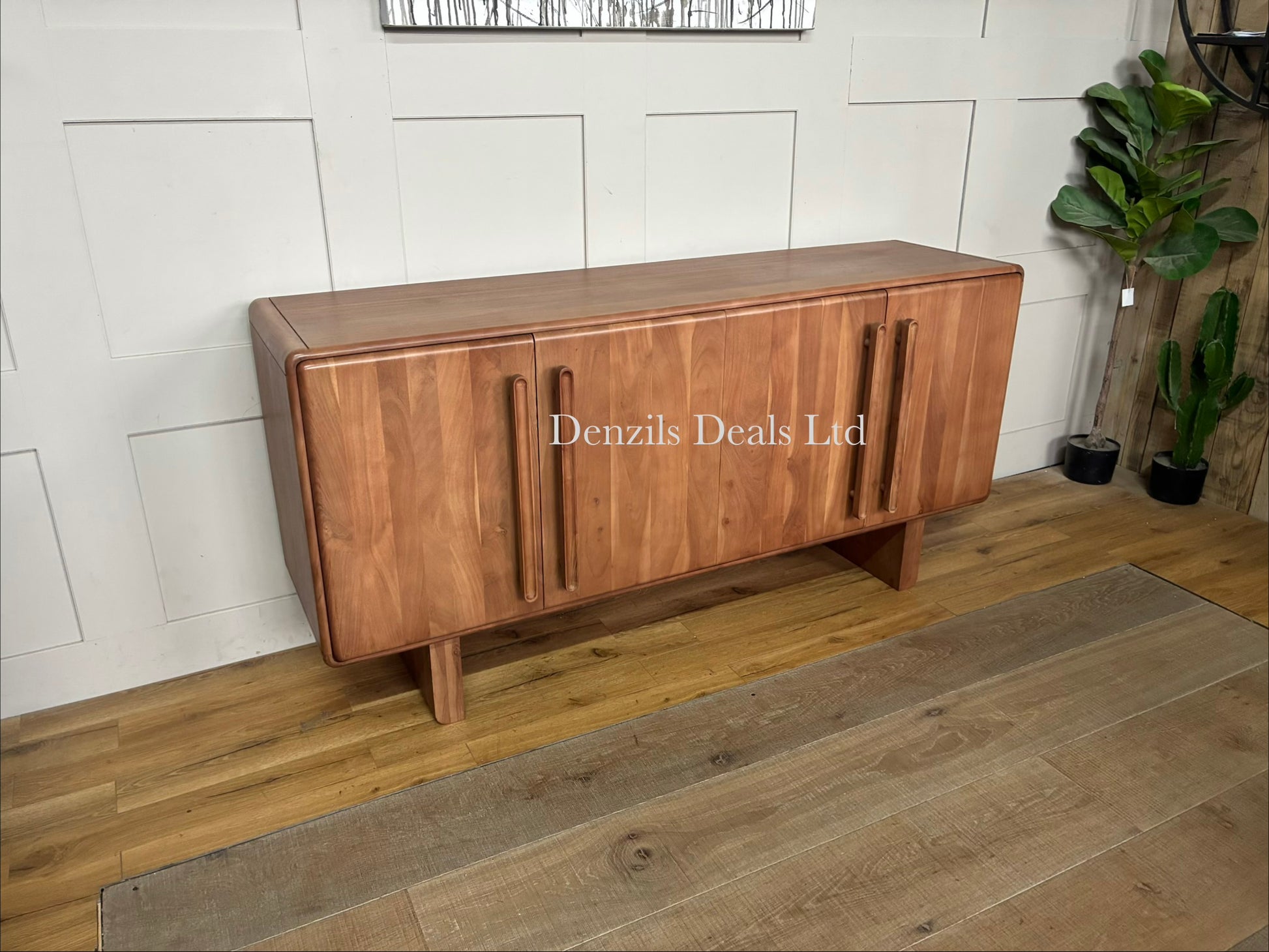 A wide, natural-finish acacia wood sideboard with four doors featuring a distinct panelled design. The furniture piece exhibits a warm wood grain, softly rounded corners, and a seamless, modern profile standing flat on the floor.